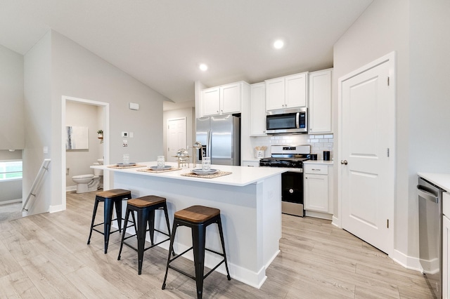 kitchen with white cabinets, appliances with stainless steel finishes, a kitchen island with sink, and a breakfast bar area