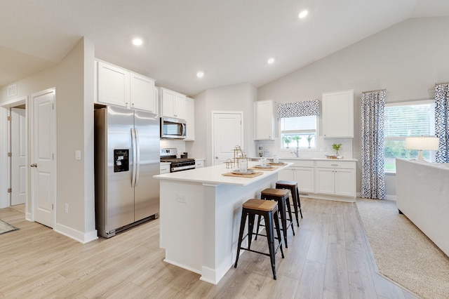 kitchen featuring lofted ceiling, white cabinets, an island with sink, appliances with stainless steel finishes, and light hardwood / wood-style floors