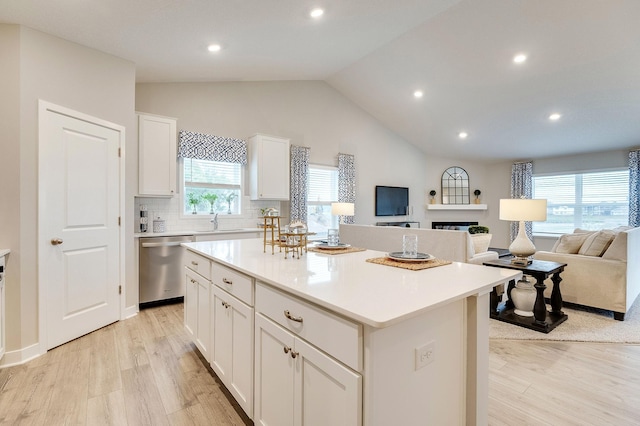 kitchen featuring white cabinetry, light hardwood / wood-style flooring, dishwasher, a kitchen island, and lofted ceiling