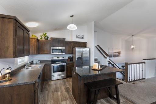 kitchen featuring stainless steel appliances, vaulted ceiling, pendant lighting, hardwood / wood-style flooring, and a center island