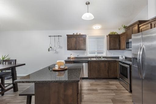 kitchen featuring dark stone counters, dark brown cabinets, stainless steel appliances, sink, and hanging light fixtures