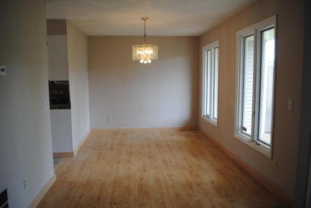 spare room featuring an inviting chandelier, light wood-type flooring, and a healthy amount of sunlight