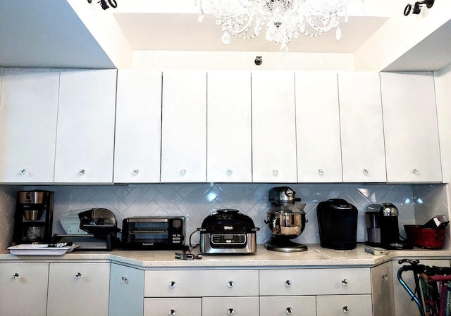 kitchen featuring white cabinets, a notable chandelier, and backsplash