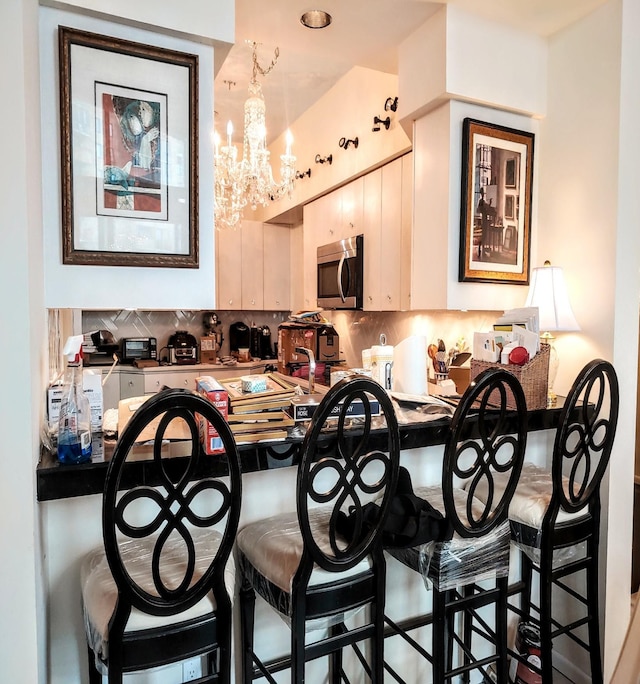 kitchen with kitchen peninsula, an inviting chandelier, a breakfast bar, and tasteful backsplash