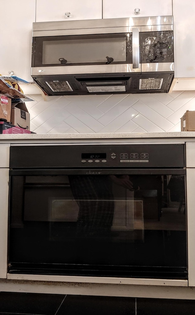 room details featuring oven, decorative backsplash, and white cabinetry