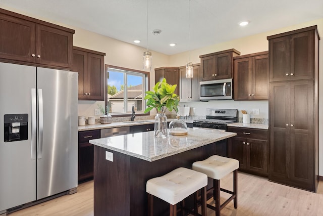 kitchen with a center island, appliances with stainless steel finishes, pendant lighting, light stone countertops, and light hardwood / wood-style floors