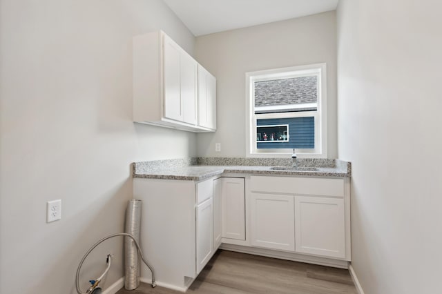 kitchen with sink, white cabinets, light stone counters, and light hardwood / wood-style flooring