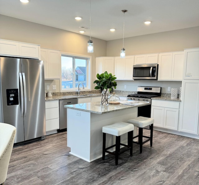 kitchen featuring wood finished floors, white cabinets, hanging light fixtures, appliances with stainless steel finishes, and a center island