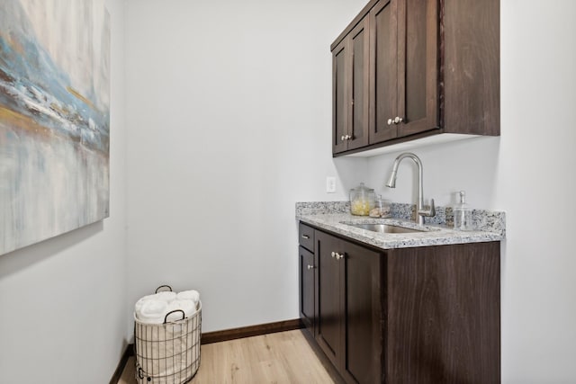 bar featuring light wood-style flooring, baseboards, and a sink