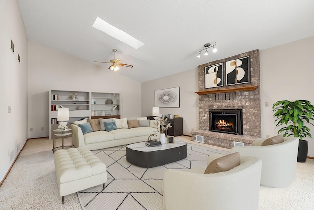 living room with carpet, ceiling fan, vaulted ceiling with skylight, and a fireplace