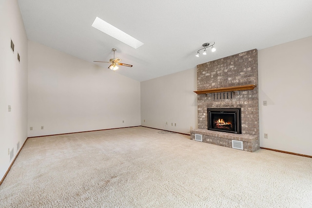 unfurnished living room featuring ceiling fan, vaulted ceiling with skylight, a brick fireplace, and carpet floors