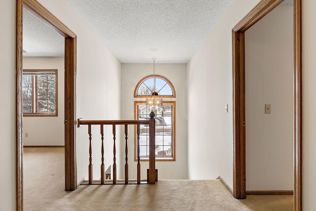 corridor with a textured ceiling, light carpet, and a chandelier