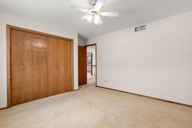 unfurnished bedroom with ceiling fan, light colored carpet, a textured ceiling, and a closet