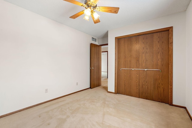 unfurnished bedroom featuring ceiling fan, light colored carpet, a textured ceiling, and a closet