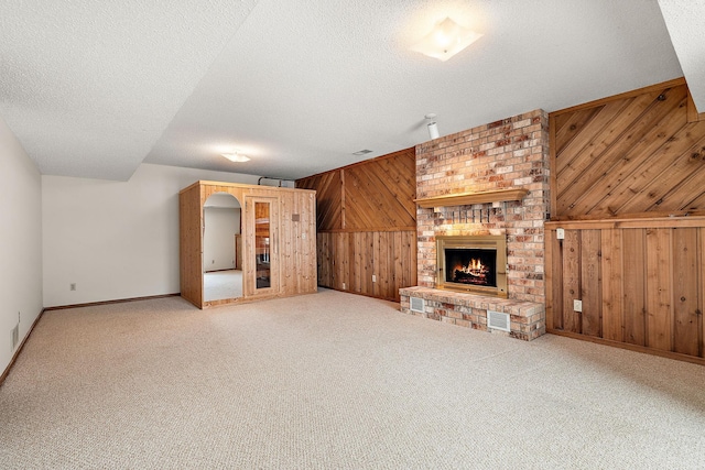 unfurnished living room featuring carpet, a brick fireplace, wooden walls, and a textured ceiling