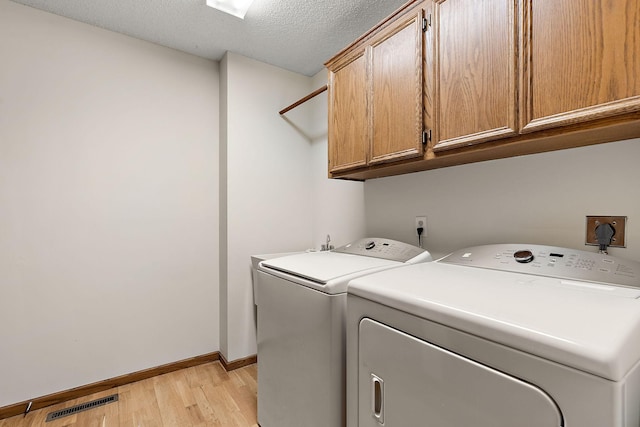 laundry area featuring light wood-type flooring, cabinets, a textured ceiling, and washer and clothes dryer