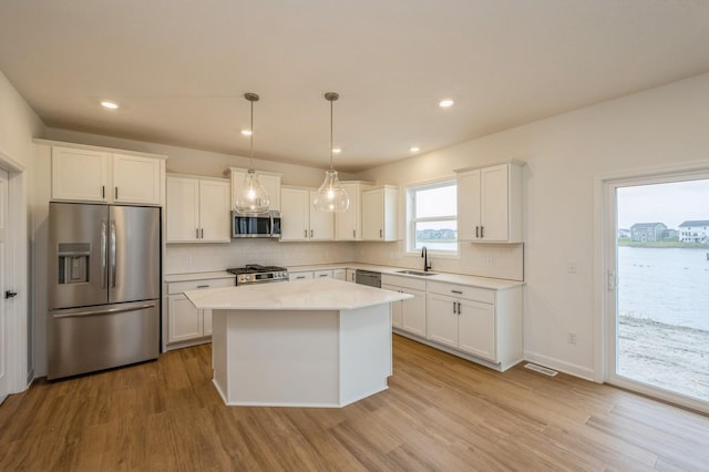 kitchen featuring white cabinets, appliances with stainless steel finishes, light wood-type flooring, and hanging light fixtures