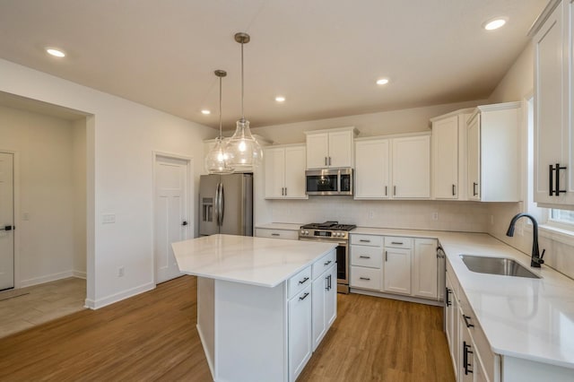 kitchen with white cabinetry, sink, appliances with stainless steel finishes, a kitchen island, and light wood-type flooring