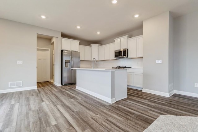 kitchen featuring a kitchen island with sink, white cabinets, stainless steel appliances, and light wood-type flooring