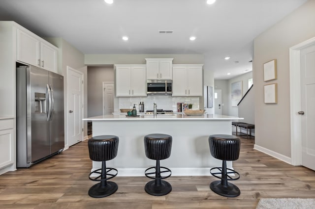 kitchen with a kitchen bar, stainless steel appliances, a center island with sink, hardwood / wood-style floors, and white cabinetry