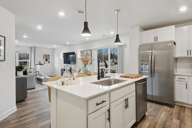 kitchen featuring sink, stainless steel appliances, decorative light fixtures, a kitchen island with sink, and white cabinets