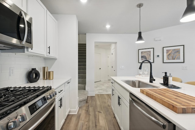 kitchen featuring sink, hanging light fixtures, light hardwood / wood-style flooring, white cabinetry, and stainless steel appliances