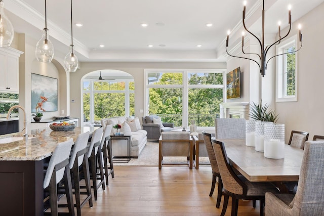 dining room with sink, crown molding, light hardwood / wood-style flooring, and a raised ceiling