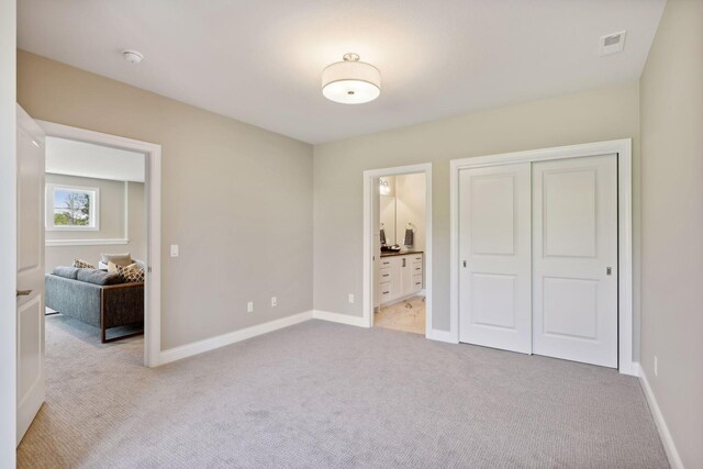 unfurnished bedroom featuring a closet, connected bathroom, and light carpet