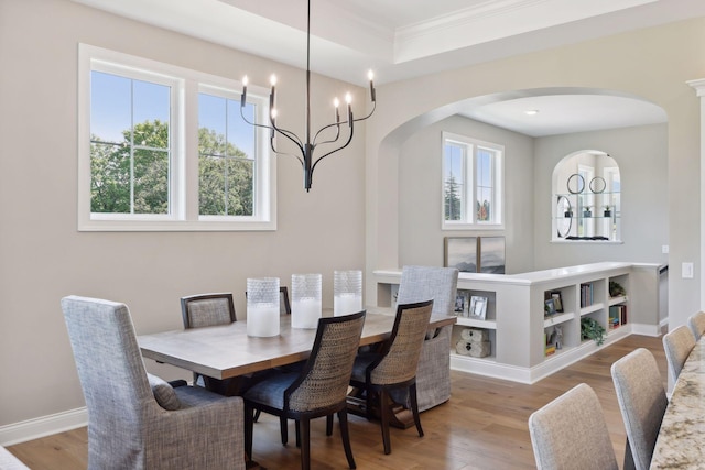 dining area featuring an inviting chandelier, ornamental molding, wood-type flooring, and a tray ceiling