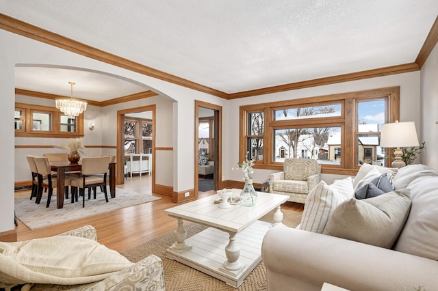 living room with an inviting chandelier, light wood-type flooring, a textured ceiling, and crown molding