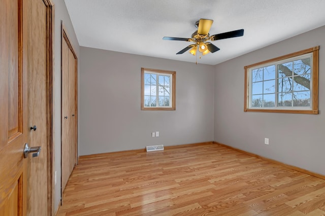 unfurnished bedroom featuring multiple windows, a textured ceiling, light hardwood / wood-style floors, and ceiling fan