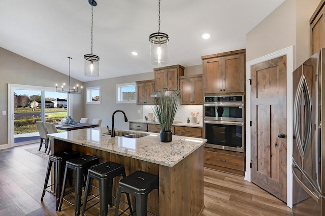 kitchen with appliances with stainless steel finishes, a kitchen island with sink, sink, decorative light fixtures, and lofted ceiling