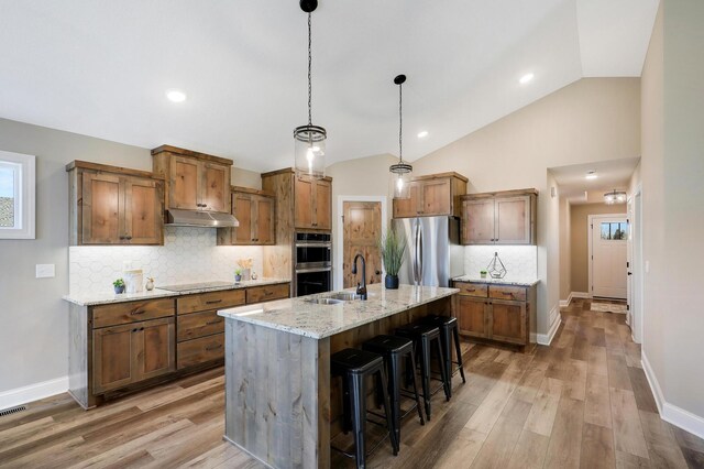 kitchen featuring a kitchen bar, a kitchen island with sink, vaulted ceiling, appliances with stainless steel finishes, and light stone counters