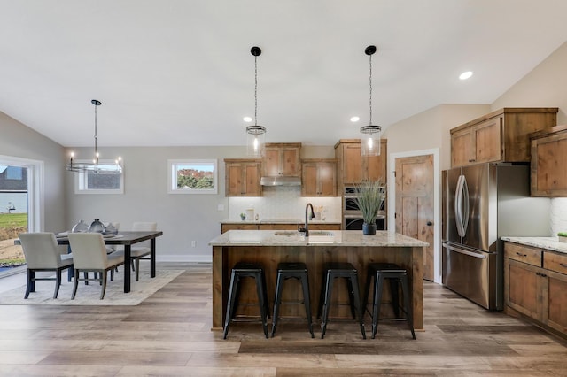 kitchen with light stone countertops, appliances with stainless steel finishes, and a kitchen island with sink