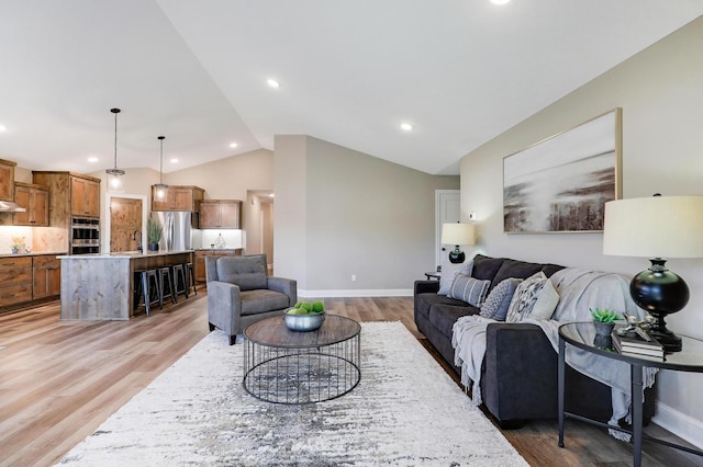 living room featuring light wood-type flooring, lofted ceiling, and sink