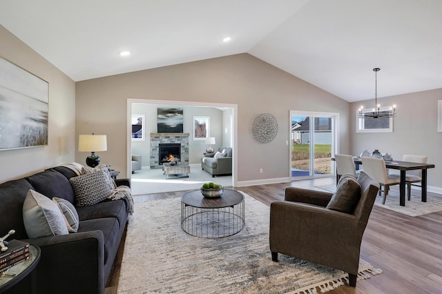 living room with vaulted ceiling, light wood-type flooring, a fireplace, and a chandelier