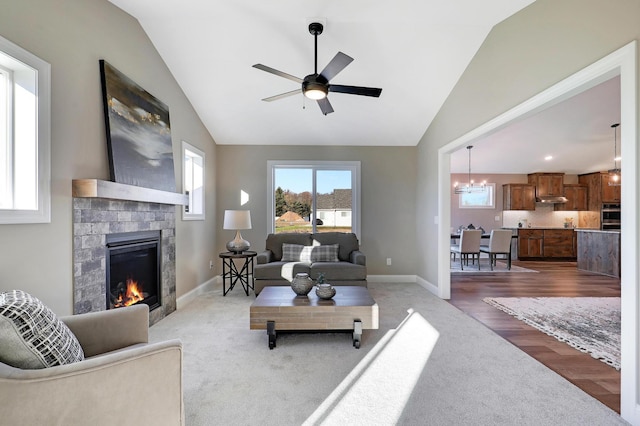 carpeted living room featuring a fireplace, ceiling fan with notable chandelier, and vaulted ceiling