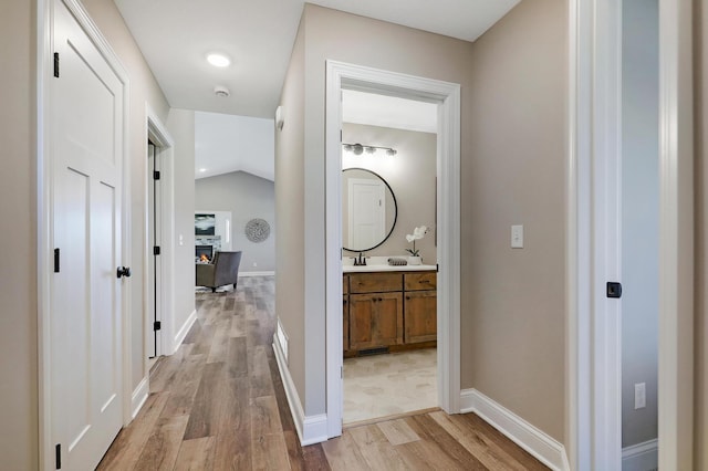 hall featuring light hardwood / wood-style floors, vaulted ceiling, and sink