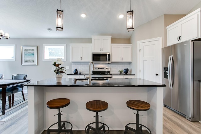 kitchen with white cabinetry, an island with sink, hanging light fixtures, and appliances with stainless steel finishes