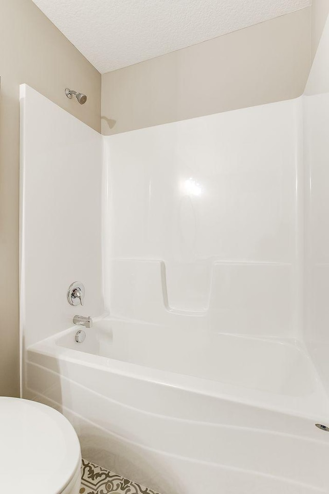 bathroom featuring tile patterned floors, shower / bathtub combination, a textured ceiling, and toilet