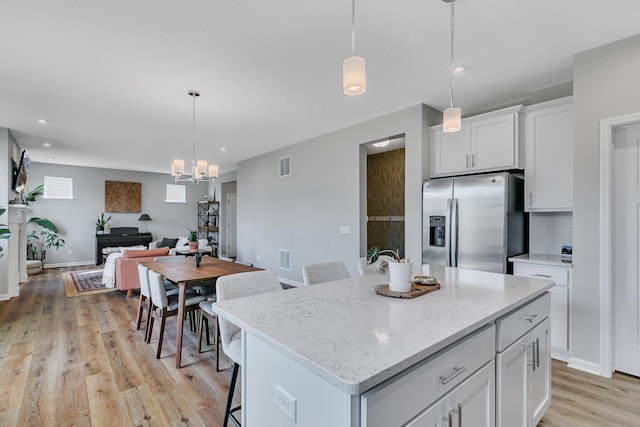 kitchen featuring pendant lighting, a center island, stainless steel fridge, tasteful backsplash, and white cabinetry