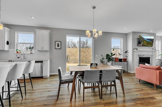 dining space featuring a high end fireplace, light wood-type flooring, an inviting chandelier, and plenty of natural light