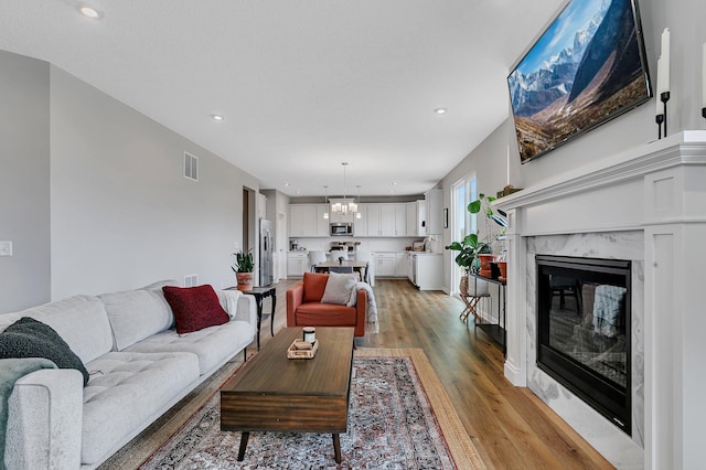 living room with a high end fireplace, a notable chandelier, and light wood-type flooring