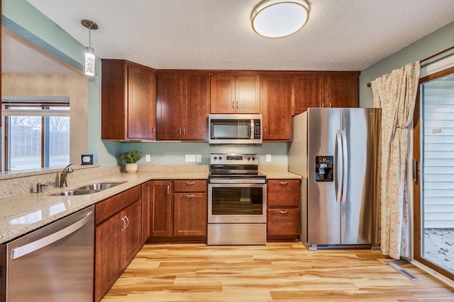 kitchen with hanging light fixtures, sink, light wood-type flooring, a textured ceiling, and appliances with stainless steel finishes