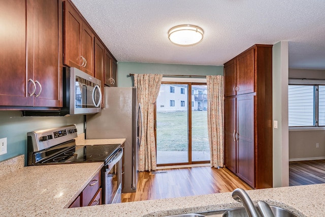 kitchen with a textured ceiling, stainless steel appliances, and light stone counters