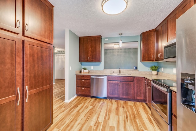 kitchen with pendant lighting, sink, a textured ceiling, appliances with stainless steel finishes, and light hardwood / wood-style floors