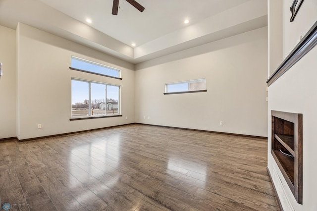 unfurnished living room featuring a towering ceiling, hardwood / wood-style flooring, and ceiling fan