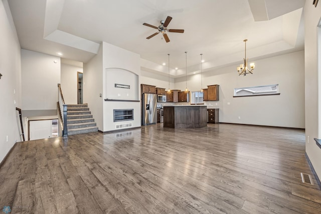 living room with dark hardwood / wood-style flooring, ceiling fan with notable chandelier, and a tray ceiling