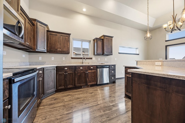 kitchen with appliances with stainless steel finishes, dark hardwood / wood-style flooring, dark brown cabinets, pendant lighting, and a notable chandelier