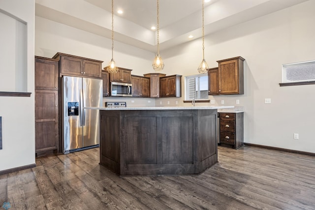 kitchen with dark wood-type flooring, a high ceiling, decorative light fixtures, a kitchen island, and stainless steel appliances